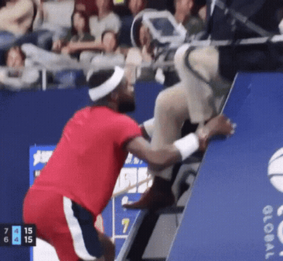 A Man In A Red Shirt Is Helping Another Man Up A Staircase GIF