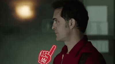 A Man In A Red Shirt Is Holding A Foam Finger In His Right Hand . GIF