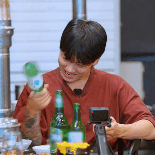 A Man In A Red Shirt Is Holding A Green Bottle Of Beer GIF
