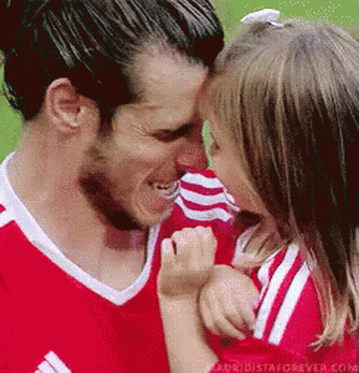 A Man In A Red Shirt Is Holding A Little Girl In His Arms And Kissing Her On The Forehead . GIF
