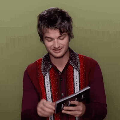 A Man In A Red Shirt Is Holding A Magazine In His Hands . GIF