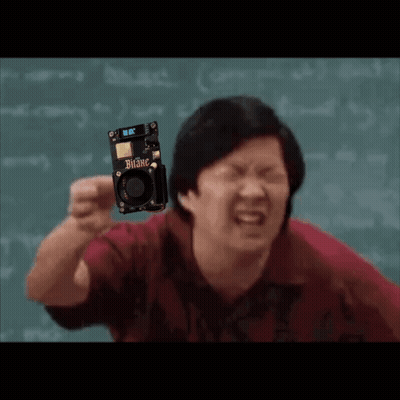 A Man In A Red Shirt Is Holding A Small Electronic Device . GIF
