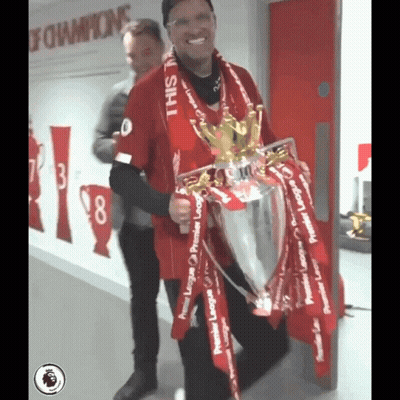 A Man In A Red Shirt Is Holding A Trophy That Says Premier League On It GIF