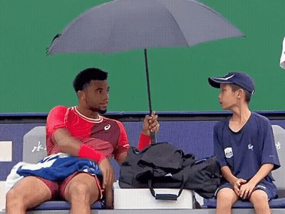 A Man In A Red Shirt Is Holding An Umbrella Over Another Man In A Blue Shirt GIF