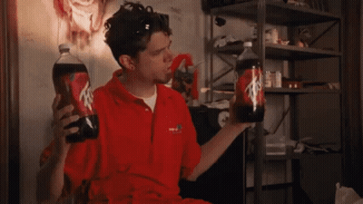 A Man In A Red Shirt Is Holding Two Bottles Of Soda One Of Which Has The Letter A On It GIF