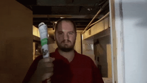 A Man In A Red Shirt Is Holding Up A Bottle Of Aerosol Spray GIF