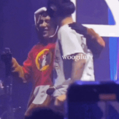 A Man In A Red Shirt Is Hugging Another Man In A White Shirt On Stage . GIF