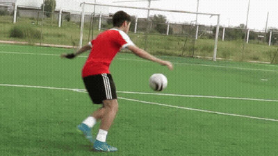 A Man In A Red Shirt Is Kicking A Soccer Ball On A Field . GIF