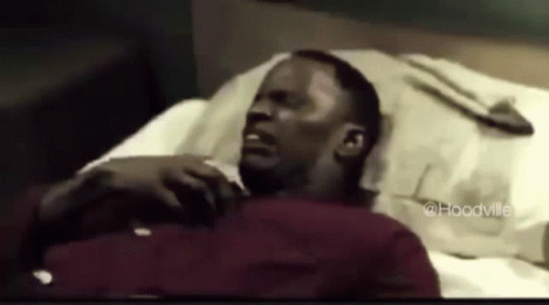 A Man In A Red Shirt Is Laying In A Bed With His Eyes Closed . GIF