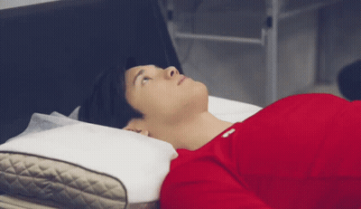 A Man In A Red Shirt Is Laying On A Bed With A Pillow And Looking Up . GIF