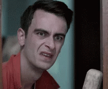 A Man In A Red Shirt Is Making A Funny Face While Leaning Against A Door . GIF