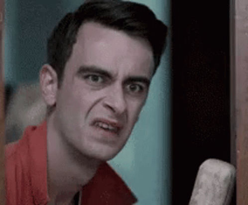 A Man In A Red Shirt Is Making A Funny Face While Standing In A Doorway . GIF