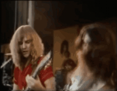 A Man In A Red Shirt Is Playing A Guitar In Front Of A Mirror While A Woman Looks On . GIF