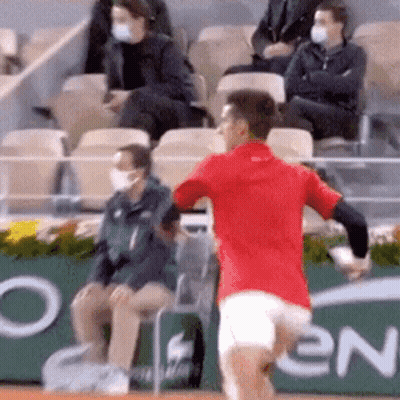 A Man In A Red Shirt Is Running On A Tennis Court In Front Of A Crowd Wearing Masks . GIF