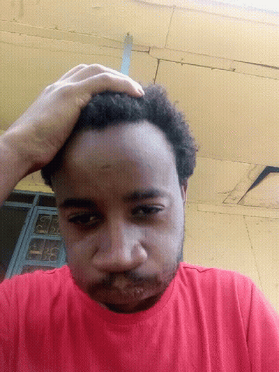 A Man In A Red Shirt Is Scratching His Head With His Hand GIF