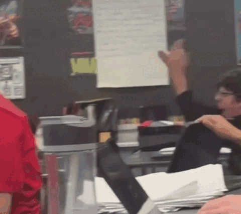 A Man In A Red Shirt Is Sitting At A Desk With A Laptop GIF