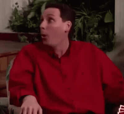 A Man In A Red Shirt Is Sitting In A Chair And Making A Funny Face . GIF