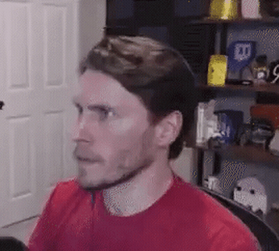 A Man In A Red Shirt Is Sitting In A Chair In Front Of A Computer . GIF