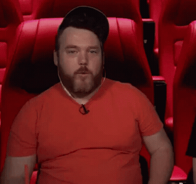 A Man In A Red Shirt Is Sitting In A Red Chair And Making A Kaboom Gesture GIF