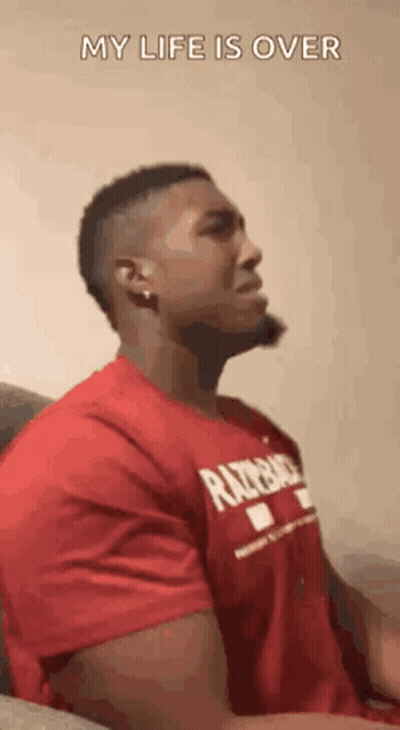A Man In A Red Shirt Is Sitting On A Couch And Making A Face . GIF