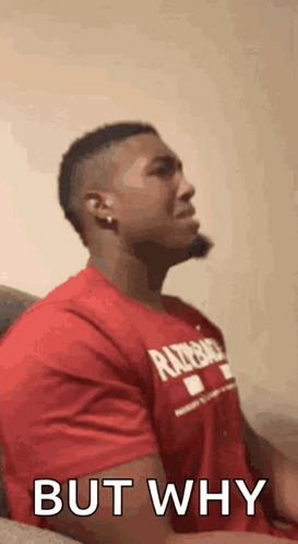 A Man In A Red Shirt Is Sitting On A Couch And Making A Face . GIF
