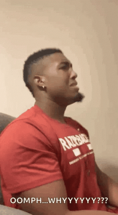 A Man In A Red Shirt Is Sitting On A Couch And Making A Funny Face . GIF