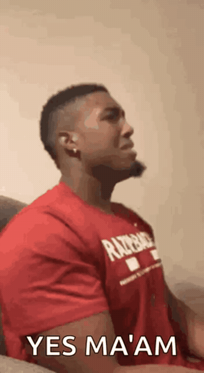 A Man In A Red Shirt Is Sitting On A Couch With His Eyes Closed And A Beard . GIF