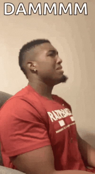 A Man In A Red Shirt Is Sitting On A Couch With His Eyes Closed And The Words Dammmm Written Above Him . GIF
