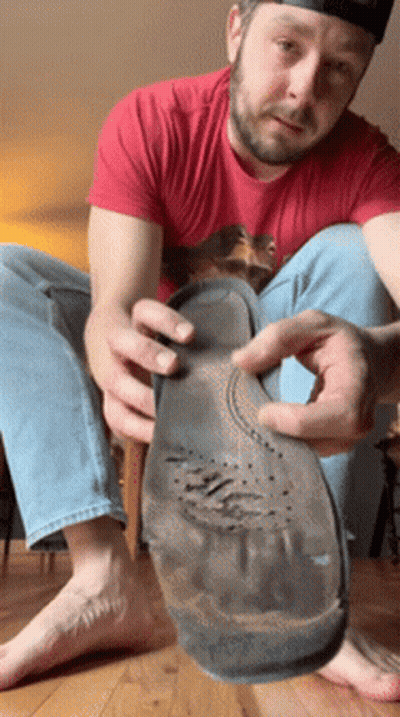 A Man In A Red Shirt Is Sitting On The Floor Holding A Shoe Sole GIF