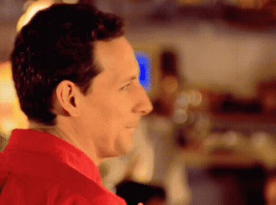 A Man In A Red Shirt Is Smiling And Looking Away From The Camera GIF