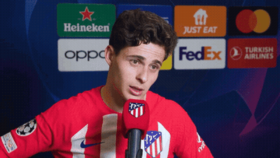 A Man In A Red Shirt Is Speaking Into A Microphone In Front Of A Heineken Logo GIF