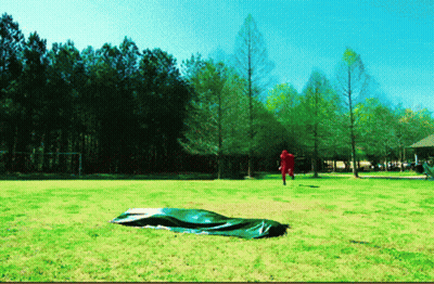 A Man In A Red Shirt Is Standing In A Field With Trees In The Background GIF