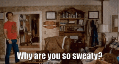 A Man In A Red Shirt Is Standing In A Living Room Asking Why Are You So Sweaty . GIF