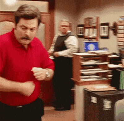 A Man In A Red Shirt Is Standing In A Room GIF
