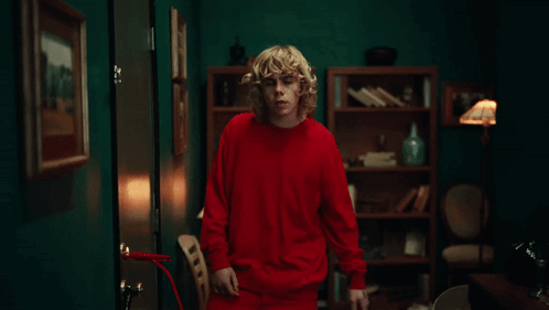 A Man In A Red Shirt Is Standing In A Room GIF