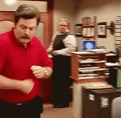 A Man In A Red Shirt Is Standing In A Room With Other Men GIF