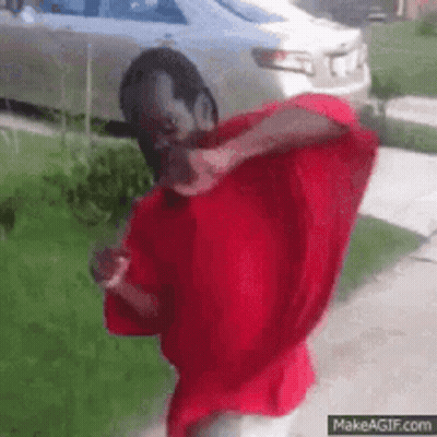A Man In A Red Shirt Is Standing In Front Of A Car . GIF