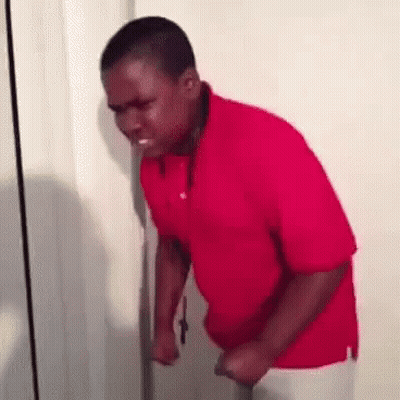 A Man In A Red Shirt Is Standing In Front Of A Door And Making A Funny Face . GIF