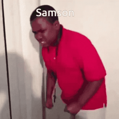 A Man In A Red Shirt Is Standing In Front Of A Door With His Fist In The Air . GIF