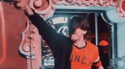A Man In A Red Shirt Is Standing In Front Of A Mirror With His Arms In The Air . GIF