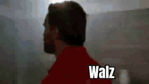 A Man In A Red Shirt Is Standing In Front Of A Mountain With The Word Walz Written On The Bottom . GIF