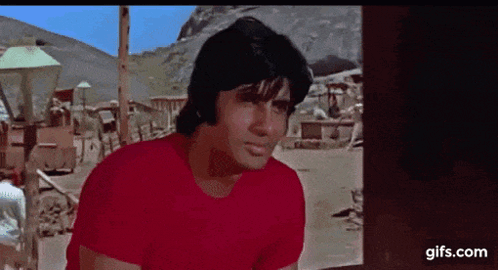 A Man In A Red Shirt Is Standing In Front Of A Window . GIF