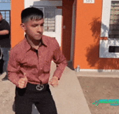 A Man In A Red Shirt Is Standing In Front Of An Orange Building With The Number 505 On It GIF