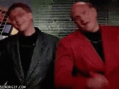 A Man In A Red Shirt Is Standing Next To Another Man In A Black Suit . GIF