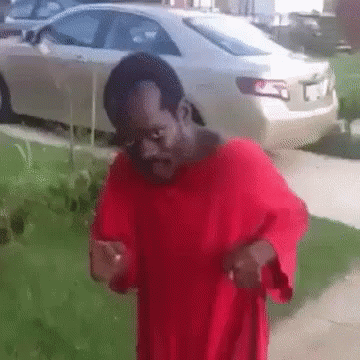 A Man In A Red Shirt Is Standing On A Sidewalk In Front Of A White Car GIF