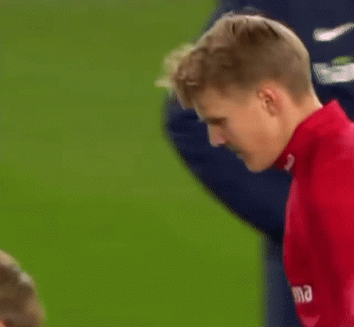 A Man In A Red Shirt Is Standing On A Soccer Field And Looking Down . GIF