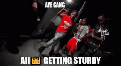 A Man In A Red Shirt Is Surrounded By A Group Of Young Men And The Caption Says Aye Gang All Getting Sturdy GIF