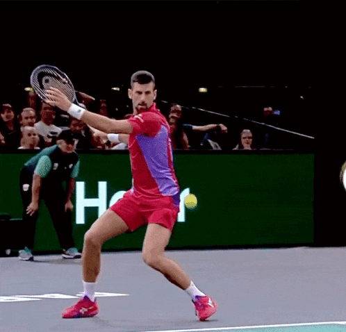 A Man In A Red Shirt Is Swinging A Tennis Racquet GIF