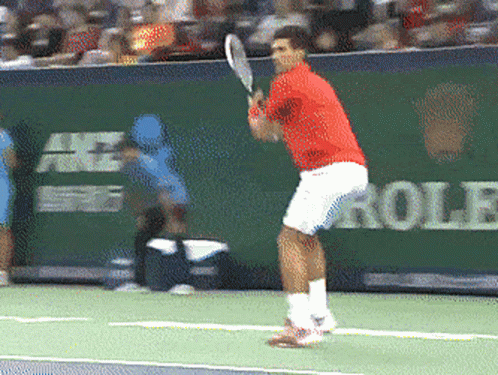 A Man In A Red Shirt Is Swinging A Tennis Racquet GIF
