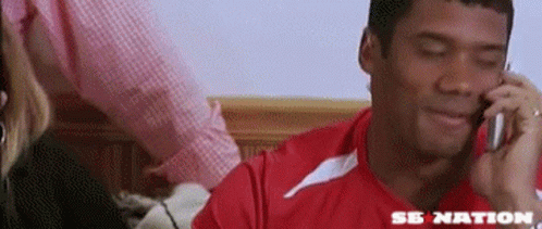 A Man In A Red Shirt Is Talking On A Cell Phone With The Word Se Nation On The Bottom GIF